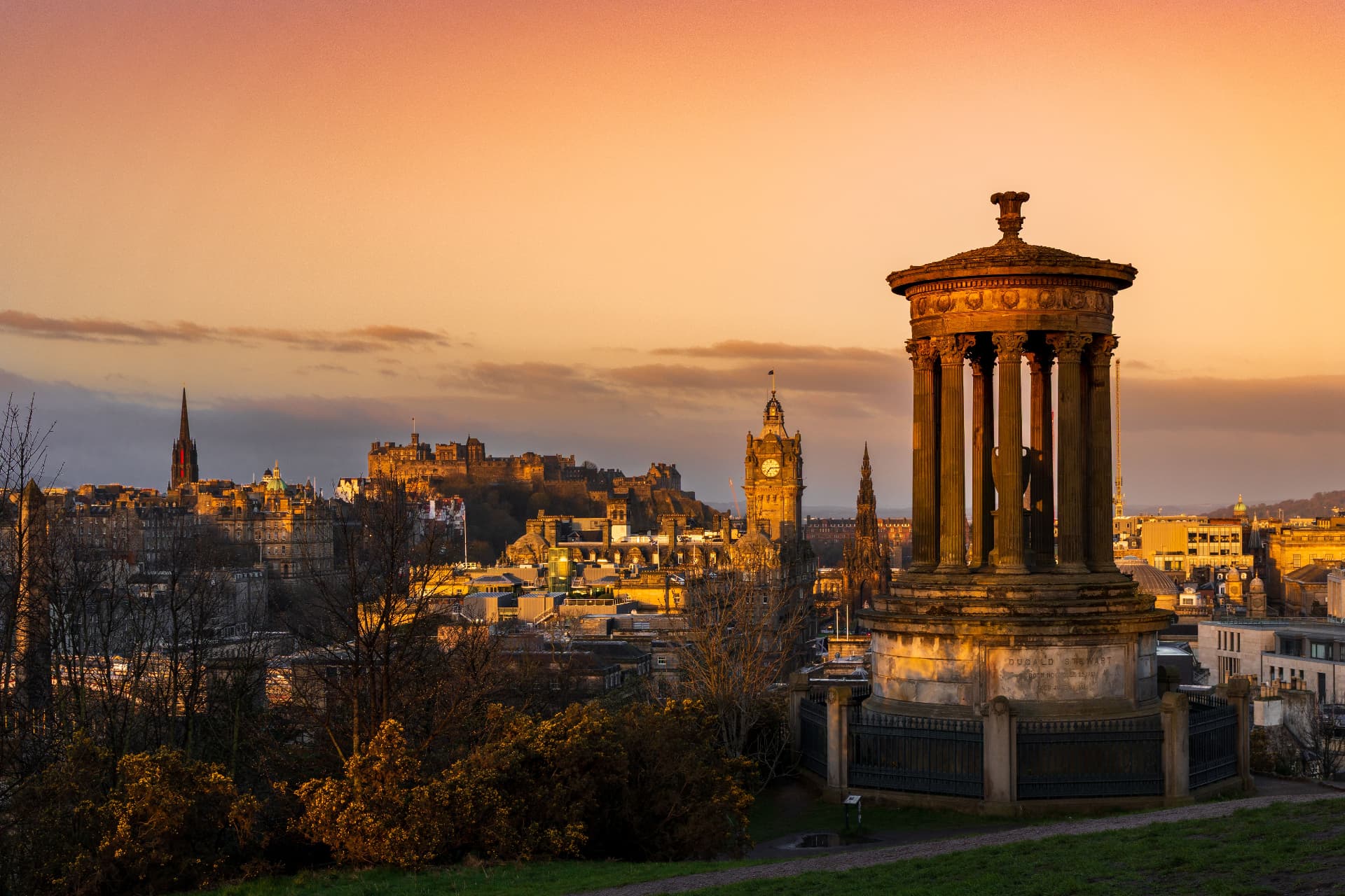 Edinburgh Castle and the city skyline at sunset, seen from Calton Hill beside the Dugald Stewart Monument